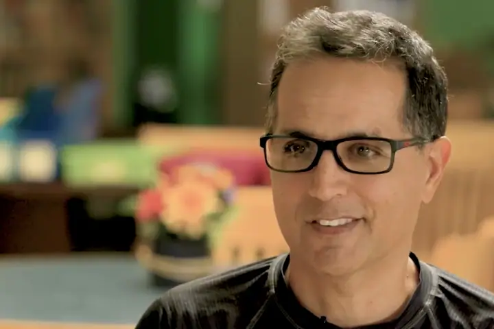 A smiling man in glasses, photographed close up indoors.