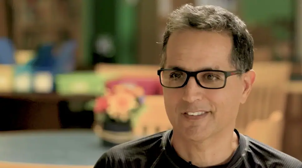 A smiling man in glasses, photographed close up indoors.