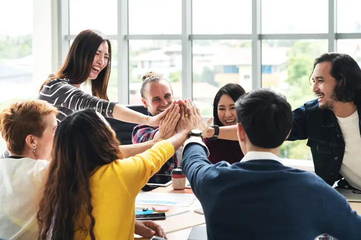 Coworkers around a conference table reach in for a group high five.