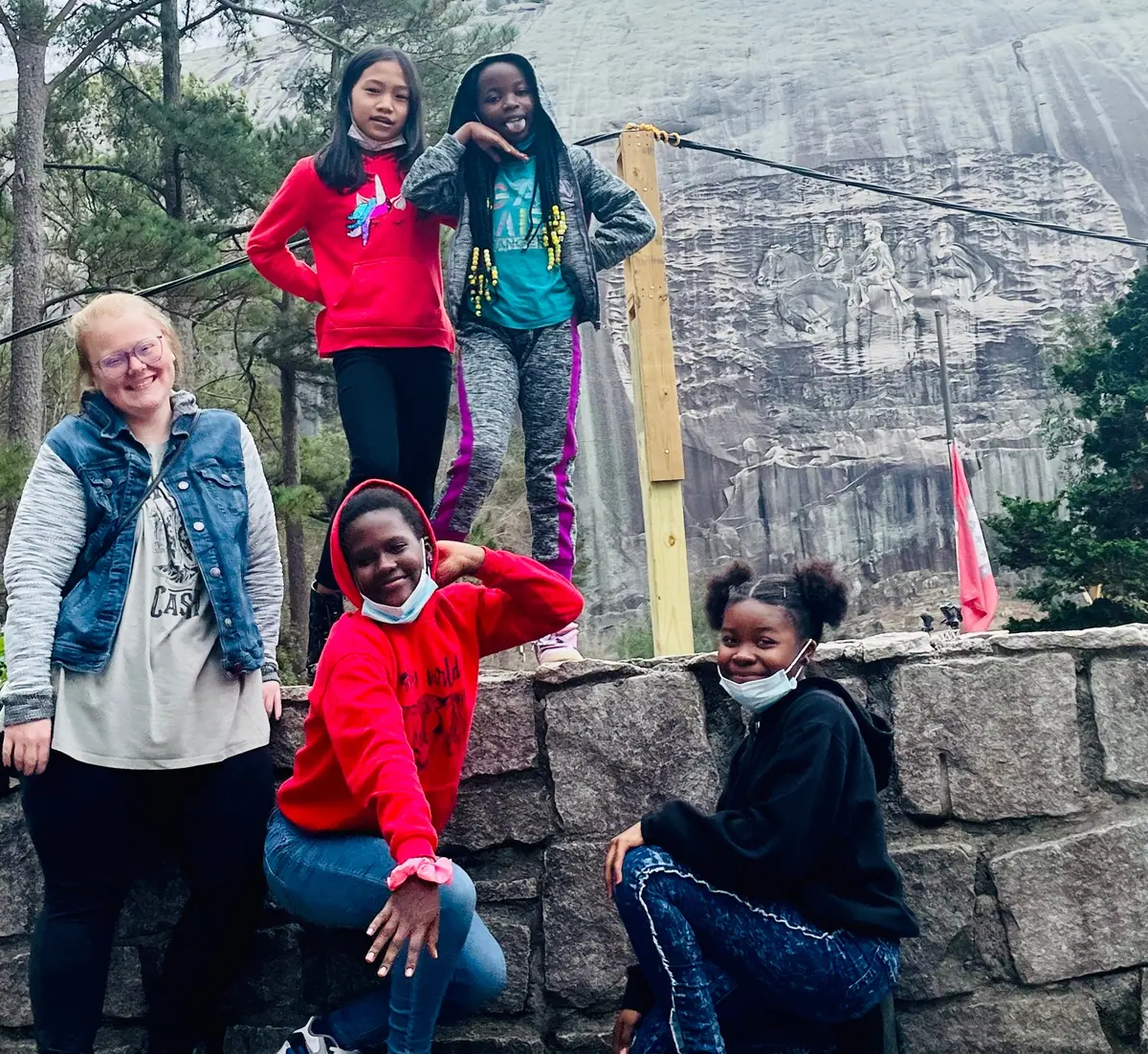 Girls and a woman pose on a stone wall below a granite mountain face.