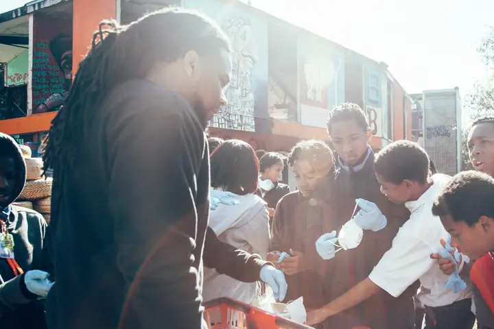 A man hands out food to a crowd of children gathered outside a food truck.
