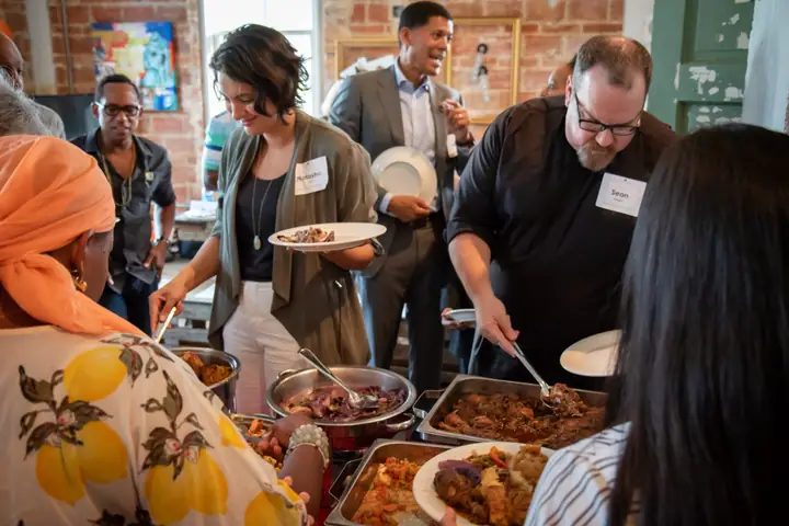 People wearing name tags serve themselves from trays of food at a community dinner.