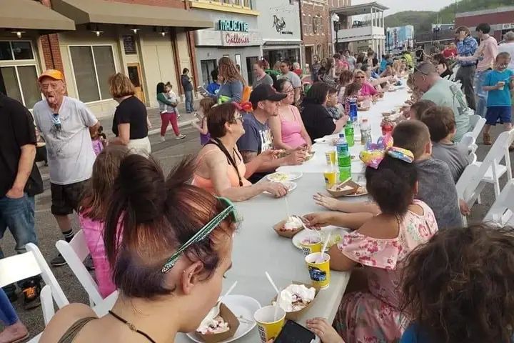 Neighbors share a meal at one long table set down the middle of a small-town main street.