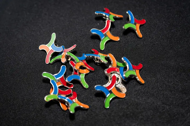 A scatter of enamel pins shaped like the four-thread Weave mark on a dark table.
