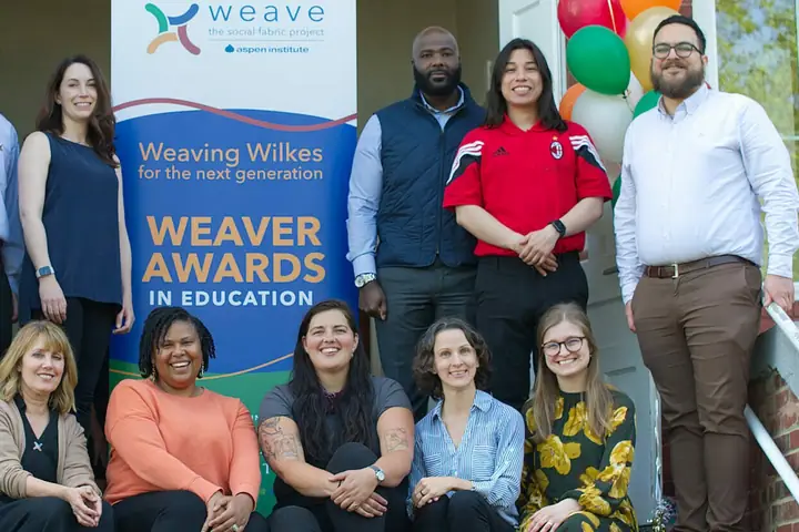 A group gathers on steps around a Weaving Wilkes Weaver Awards in Education banner.