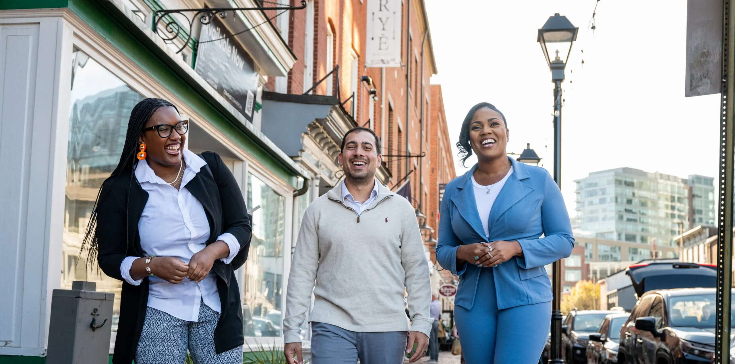 Three Baltimore Weaver Awardees laugh as they walk together down a brick-lined city street.
