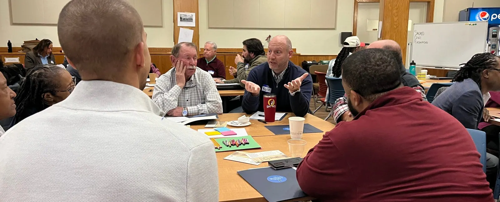 Members of a faith community talk around tables in a church fellowship hall.