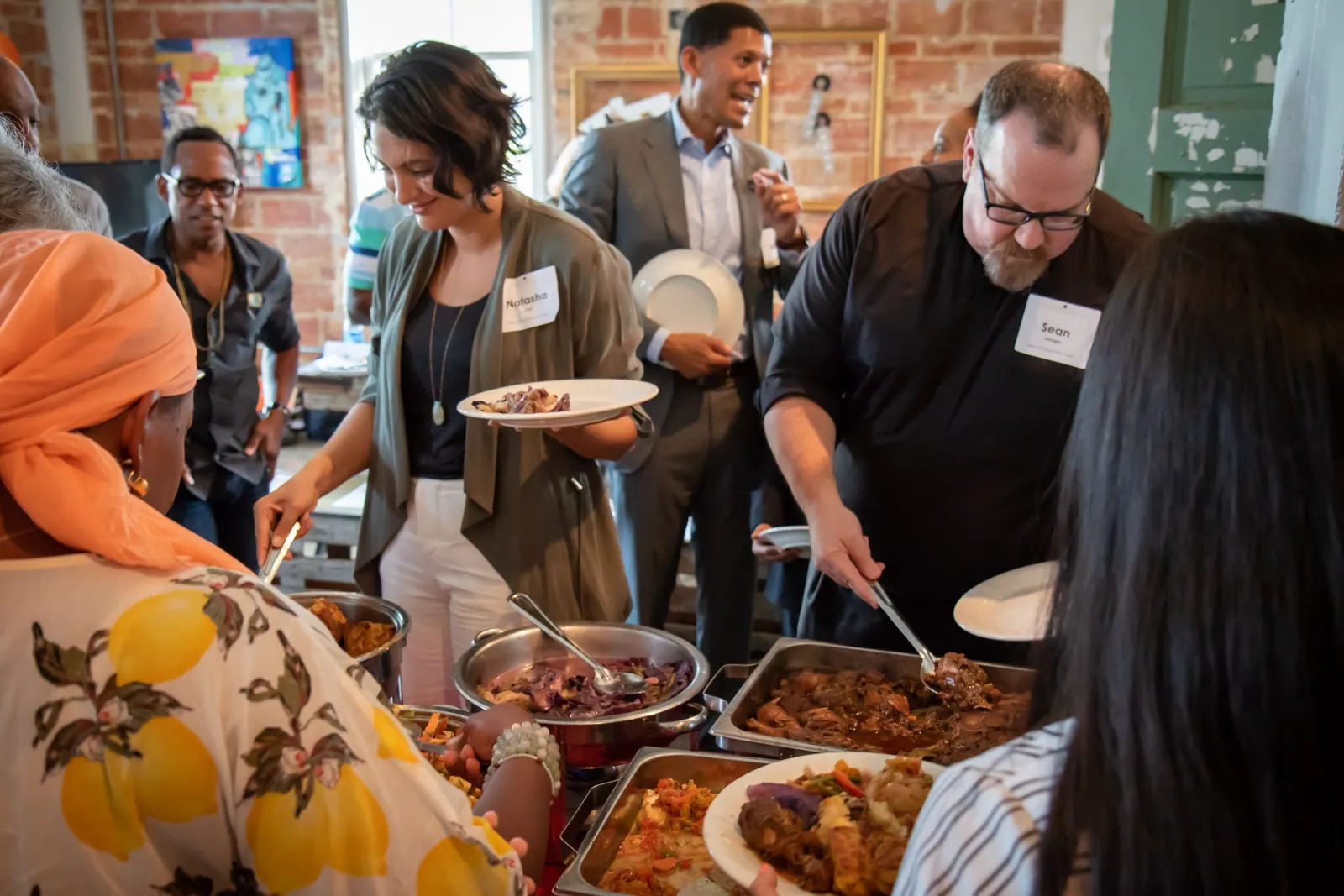 People wearing name tags serve themselves from trays of food at a community dinner.