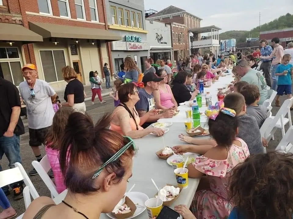 Neighbors share a meal at one long table set down the middle of a small-town main street.