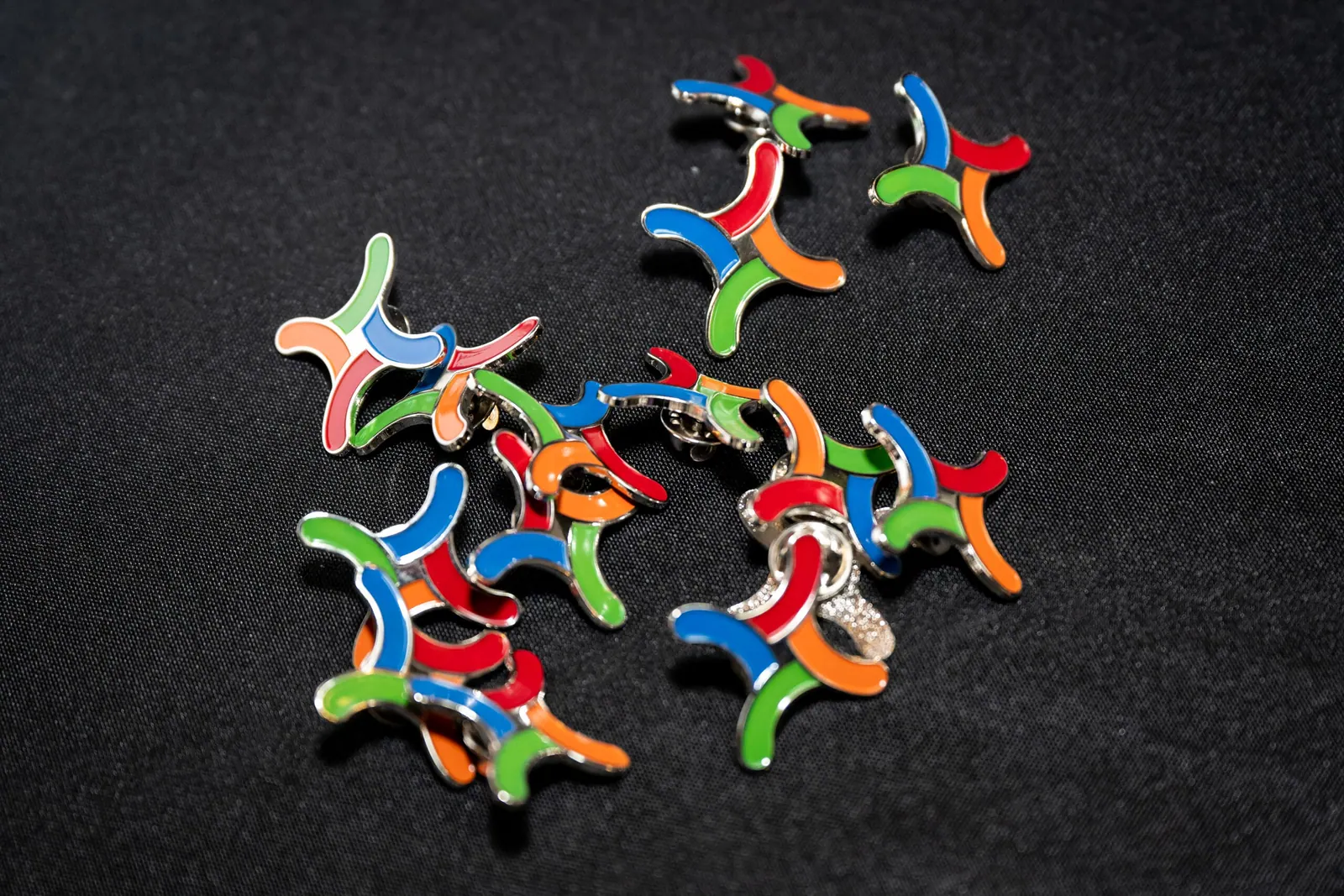 A scatter of enamel pins shaped like the four-thread Weave mark on a dark table.