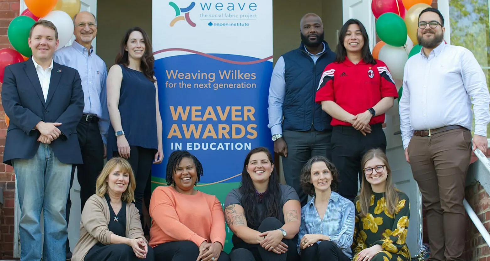 A group gathers on steps around a Weaving Wilkes Weaver Awards in Education banner.