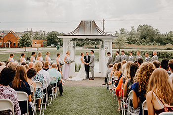 A wedding ceremony at the white gazebo, guests seated on the lawn.