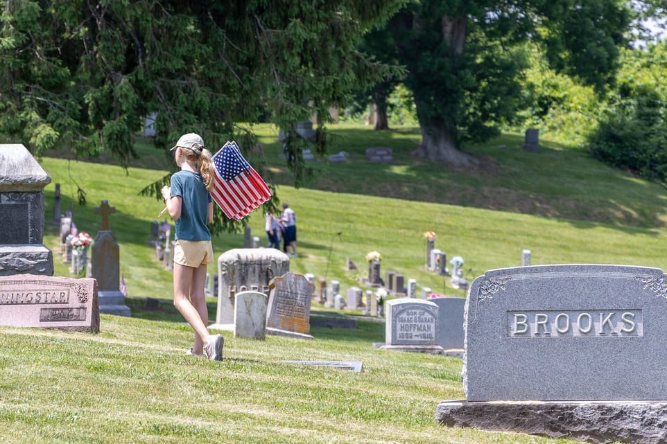 A girl carrying American flags walks among the graves at Brookside Cemetery.