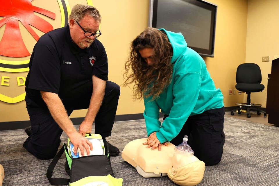 Dave Doerger of the West Chester Fire Department coaches a young woman practising CPR on a training manikin.