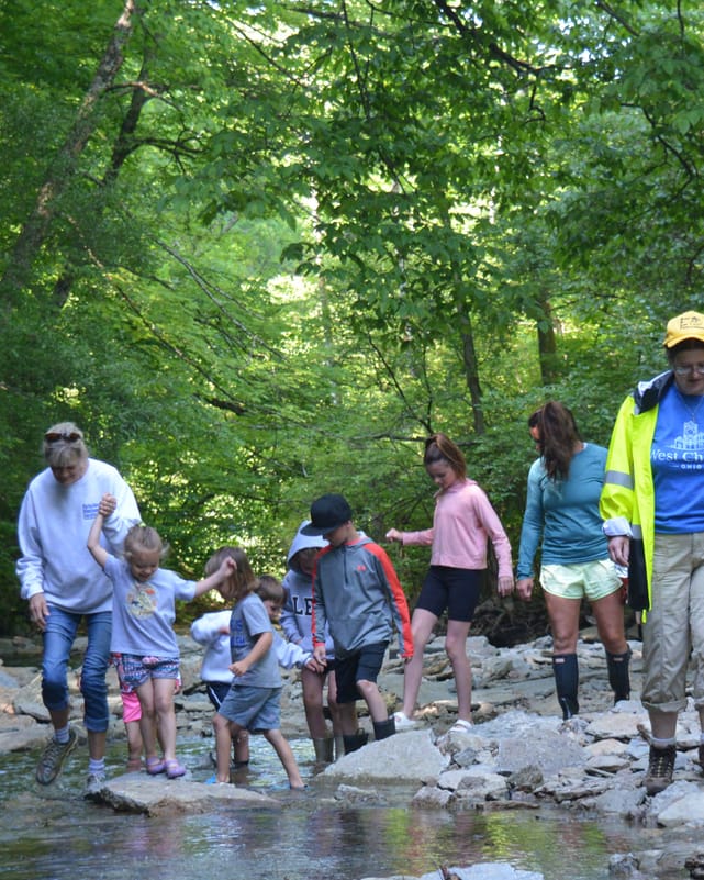 A family crosses a creek on stepping stones during a nature walk.
