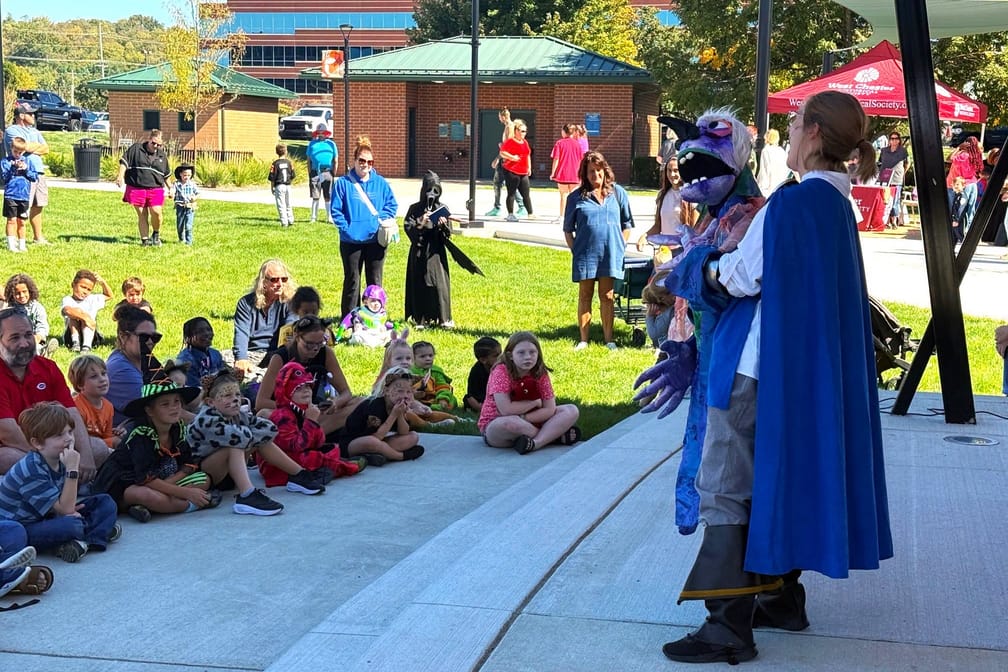 An audience sits on the grass for a Madcap Puppets show by the main stage.