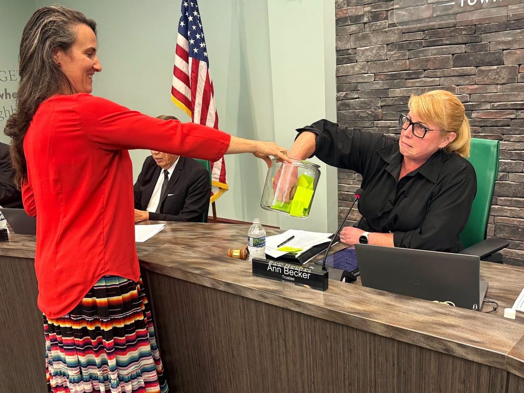 Trustee Ann Becker draws an entry from a jar held by Brianna Wooten at the Board of Trustees dais.