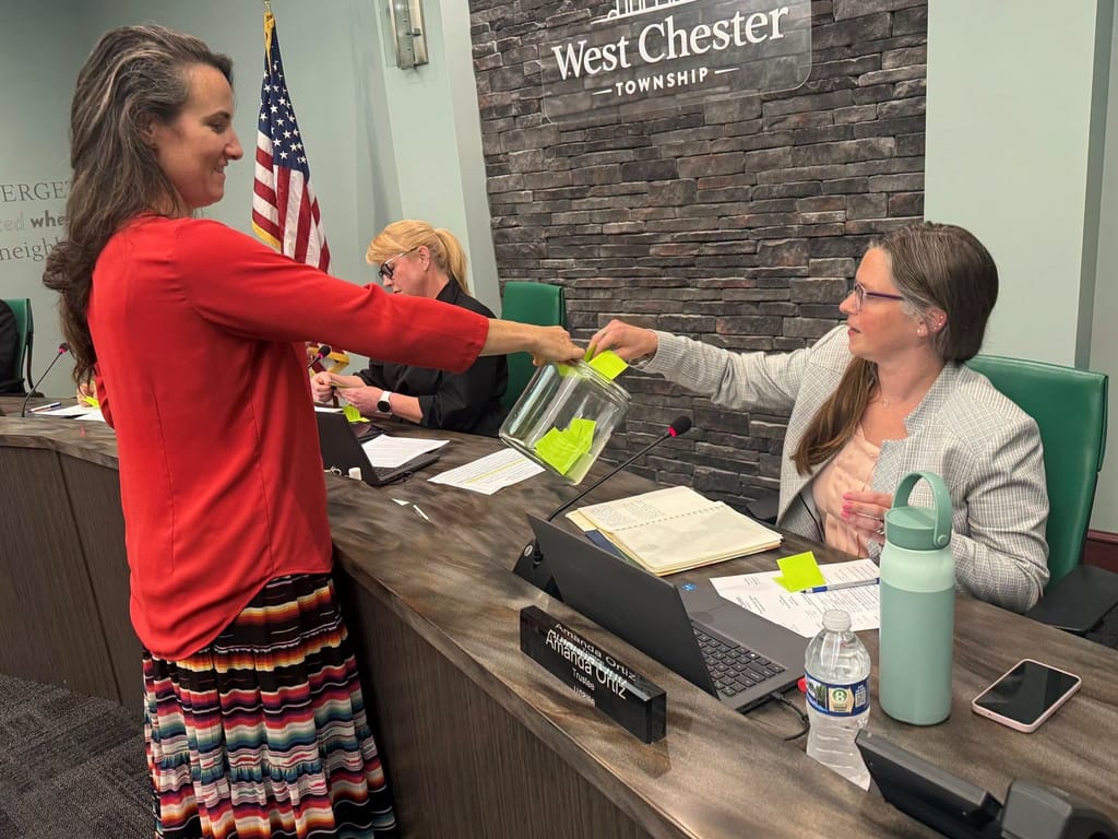 Trustee Amanda Ortiz draws a name while Brianna Wooten holds the jar at a Board of Trustees meeting.